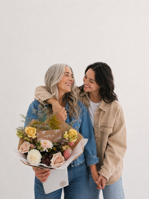 Two women smiling and holding a bouquet of Birthday flowers against a white background in Vancouver BC